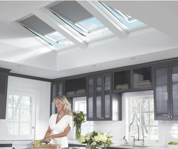 Woman preparing food in a bright modern kitchen with skylights.